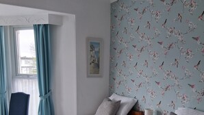 A hotel room with two beds, a chair, a nightstand with a lamp, and a floral wallpaper. - The Barbican Hotel (Paignton)