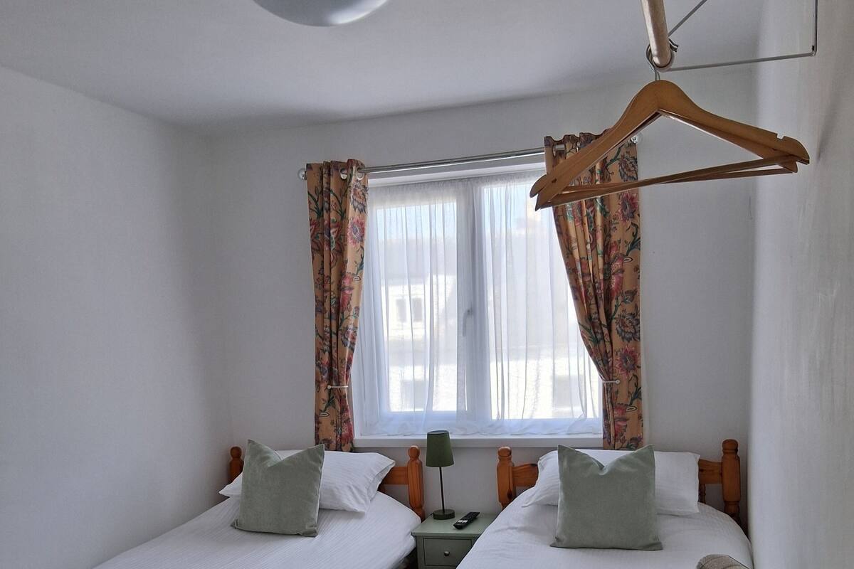 A room with two wooden beds, a bench, a hanging coat rack, and a window with curtains.