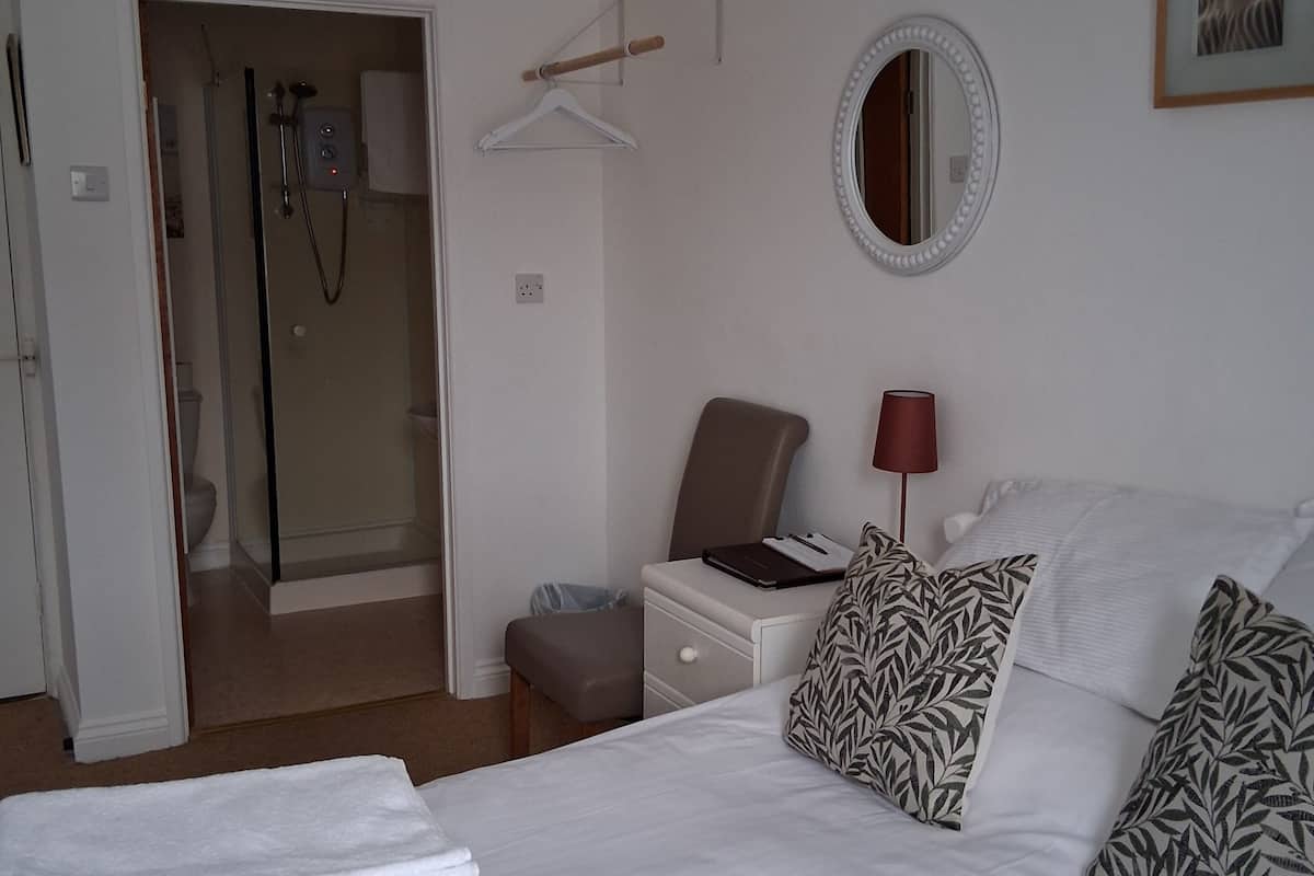 A hotel room with a bed, a bedside table, a chair, a mirror, and a bathroom visible through an open door.
