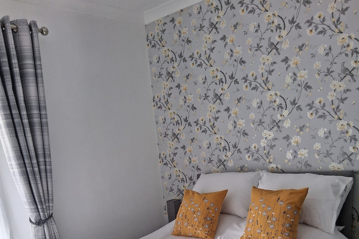 A bed with white bedding, two mustard pillows, and a floral wallpaper headboard.