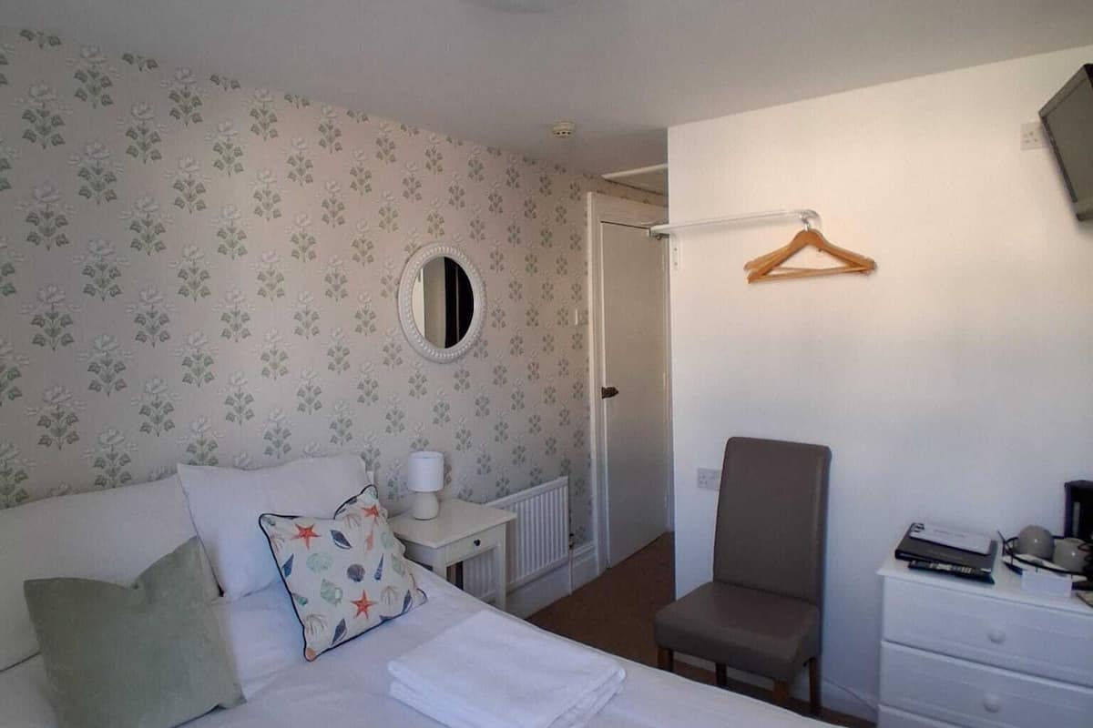 A bedroom with a bed, a chair, a dresser, a mirror, and a radiator.