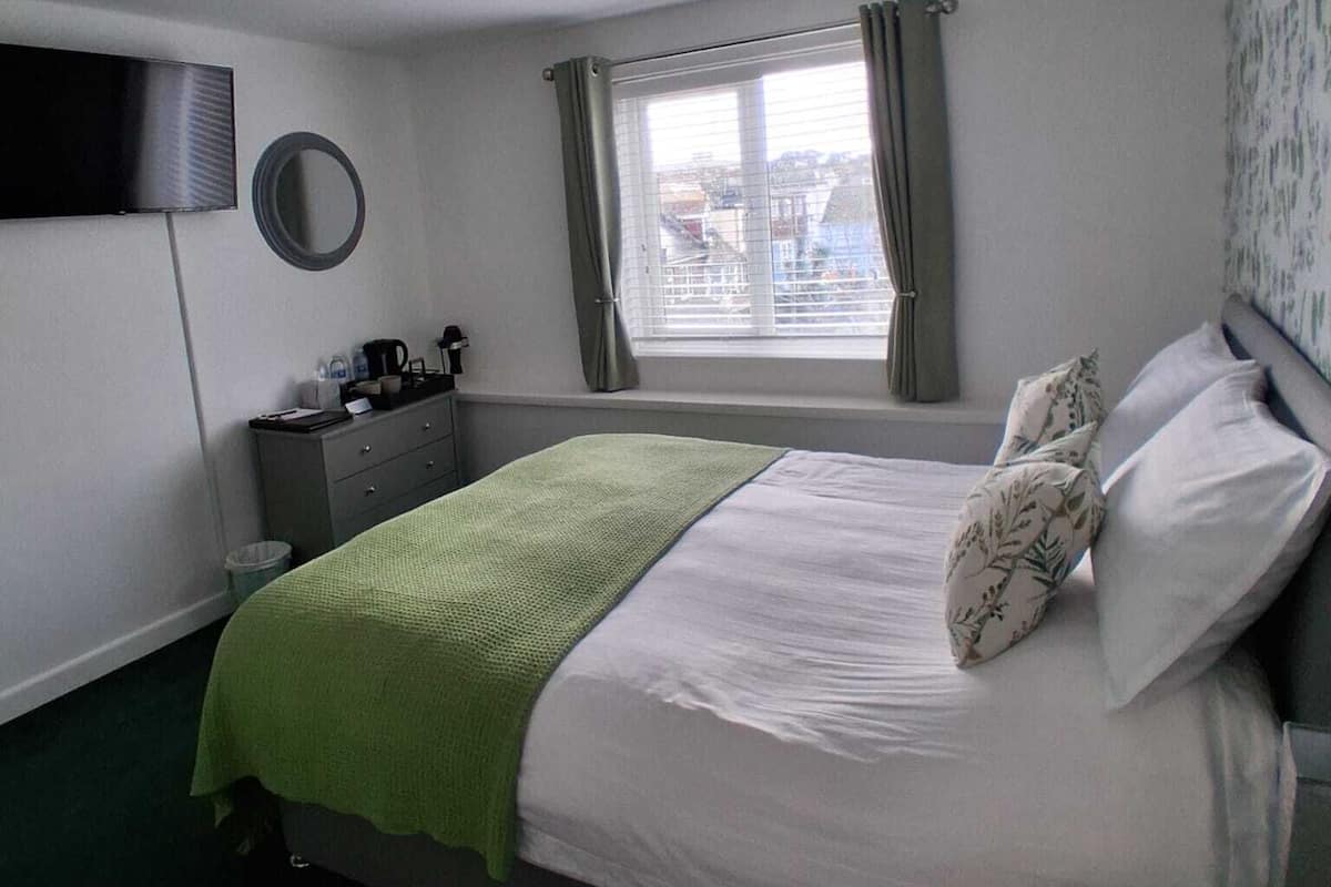A hotel room with a bed, a desk, a chair, a TV, and a window with curtains.
