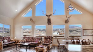Amplia sala de estar con techos altos, ventanas grandes y vista a un paisaje montañoso.
