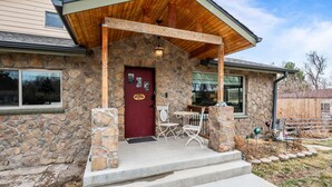 A stone house with a red door, a covered porch, and a small outdoor seating area. - Hot Tub & Gym | Minutes to Red Rocks Ampitheater | Sauna (Lakewood)