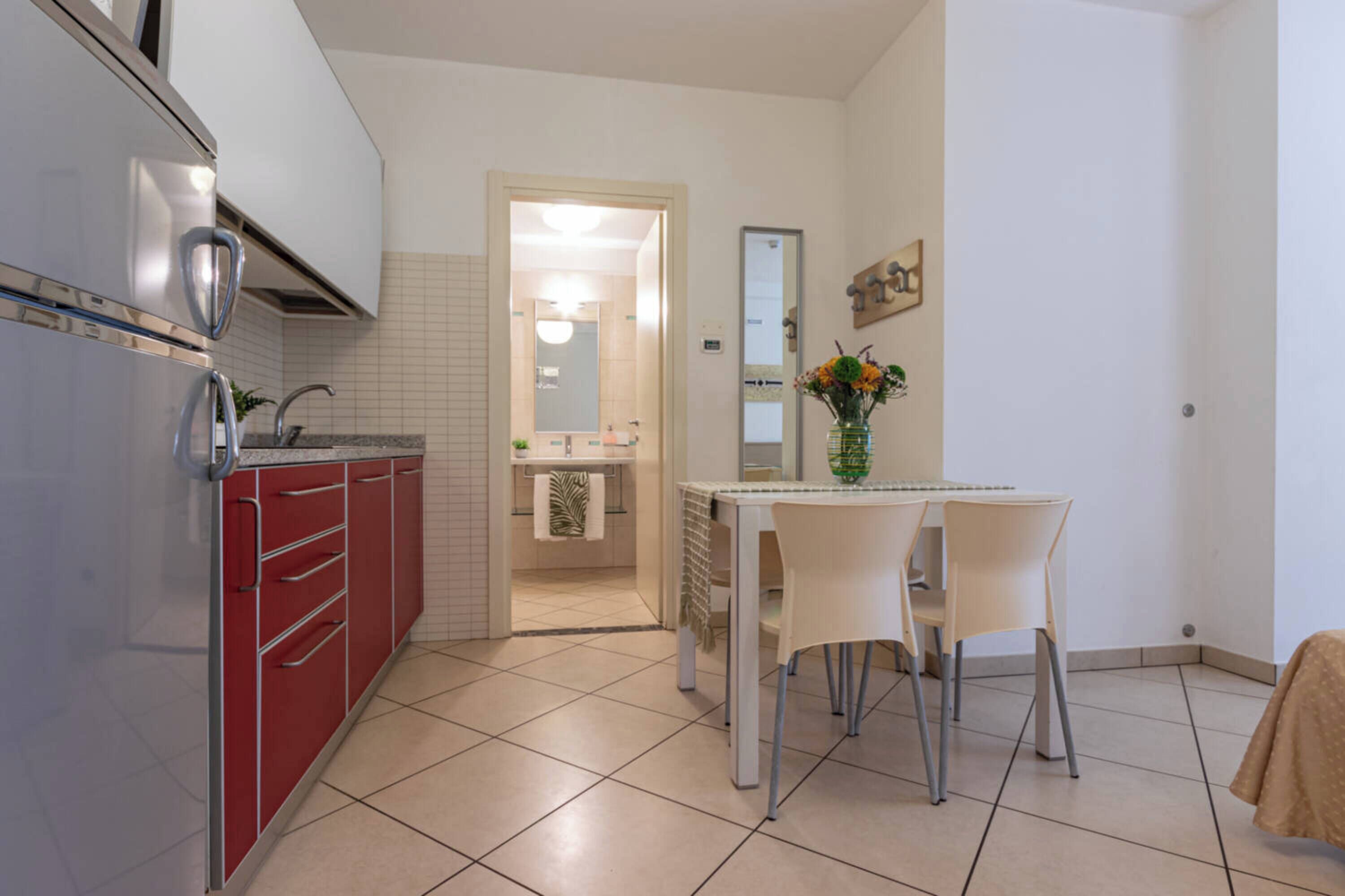 Una cocina compacta con armarios rojos, una encimera blanca y un comedor con mesa y sillas.