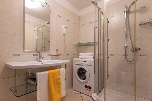 A bathroom with a sink, mirror, hairdryer, shower, and a washing machine. - Seaside Studio With Poolside Retreat (San Michele al Tagliamento)