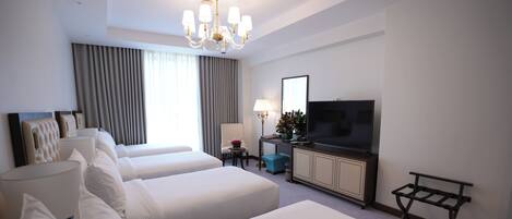 A hotel room with two beds, a TV, a desk, and a chandelier.