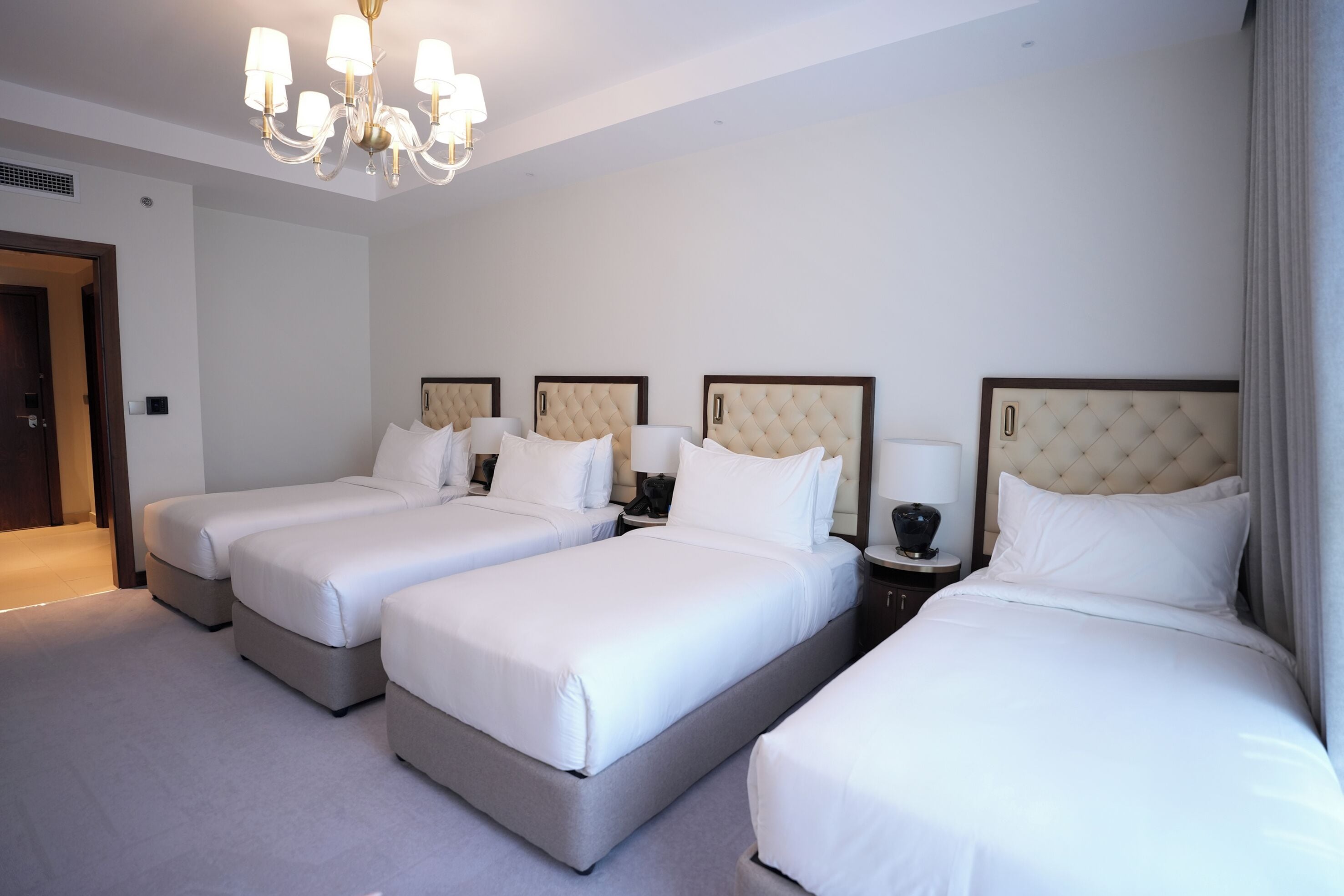 A hotel room with three beds, a chandelier, and a door.