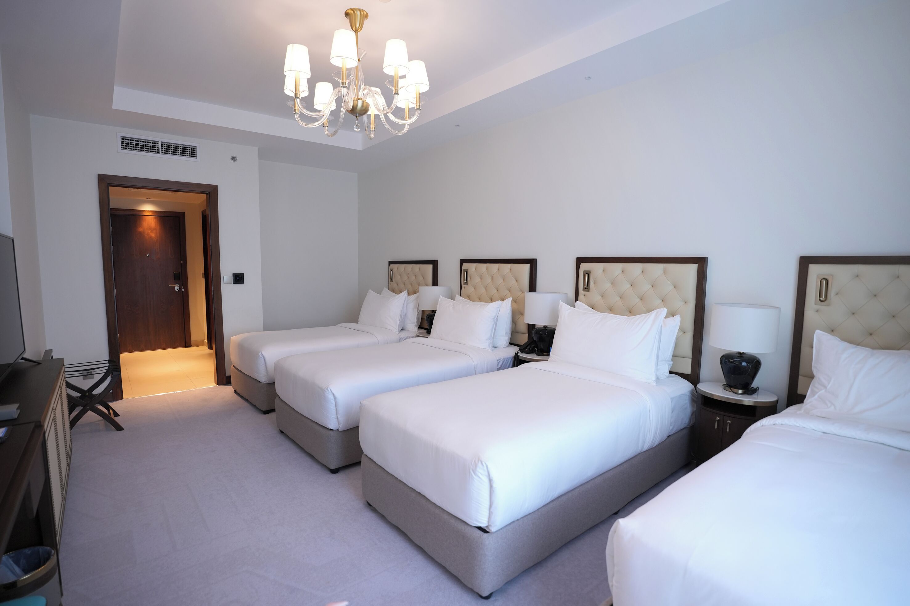 Habitación de hotel con tres camas, un candelabro, un televisor y un escritorio.
