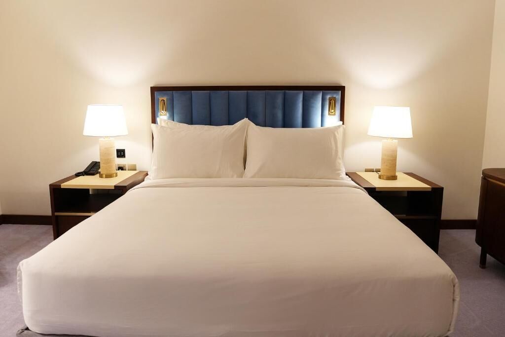 A hotel room with a large bed, two bedside tables with lamps, and a blue headboard.