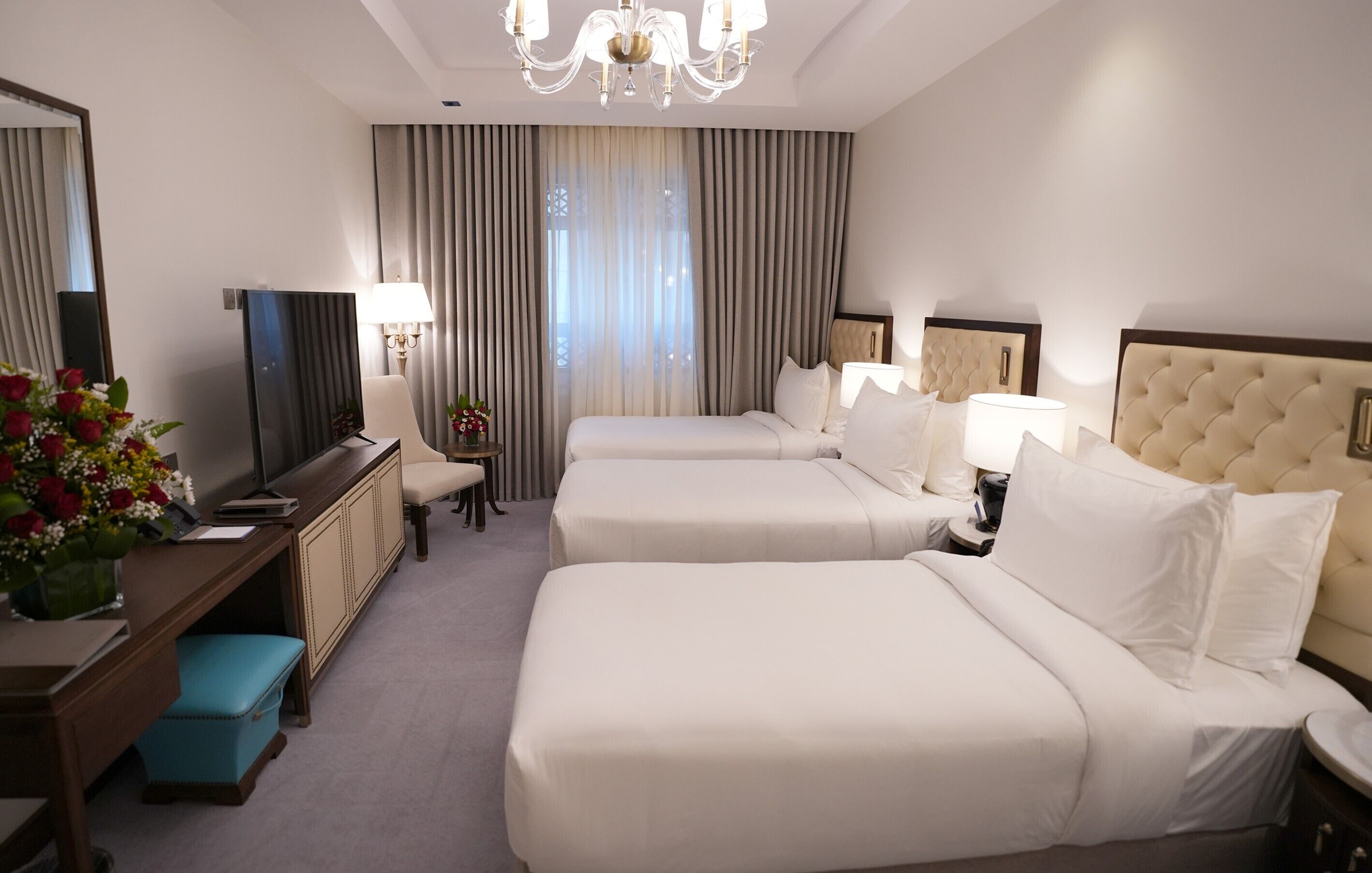 Une chambre d’hôtel avec deux lits, un bureau avec un ordinateur, une chaise, une télévision et un lustre.