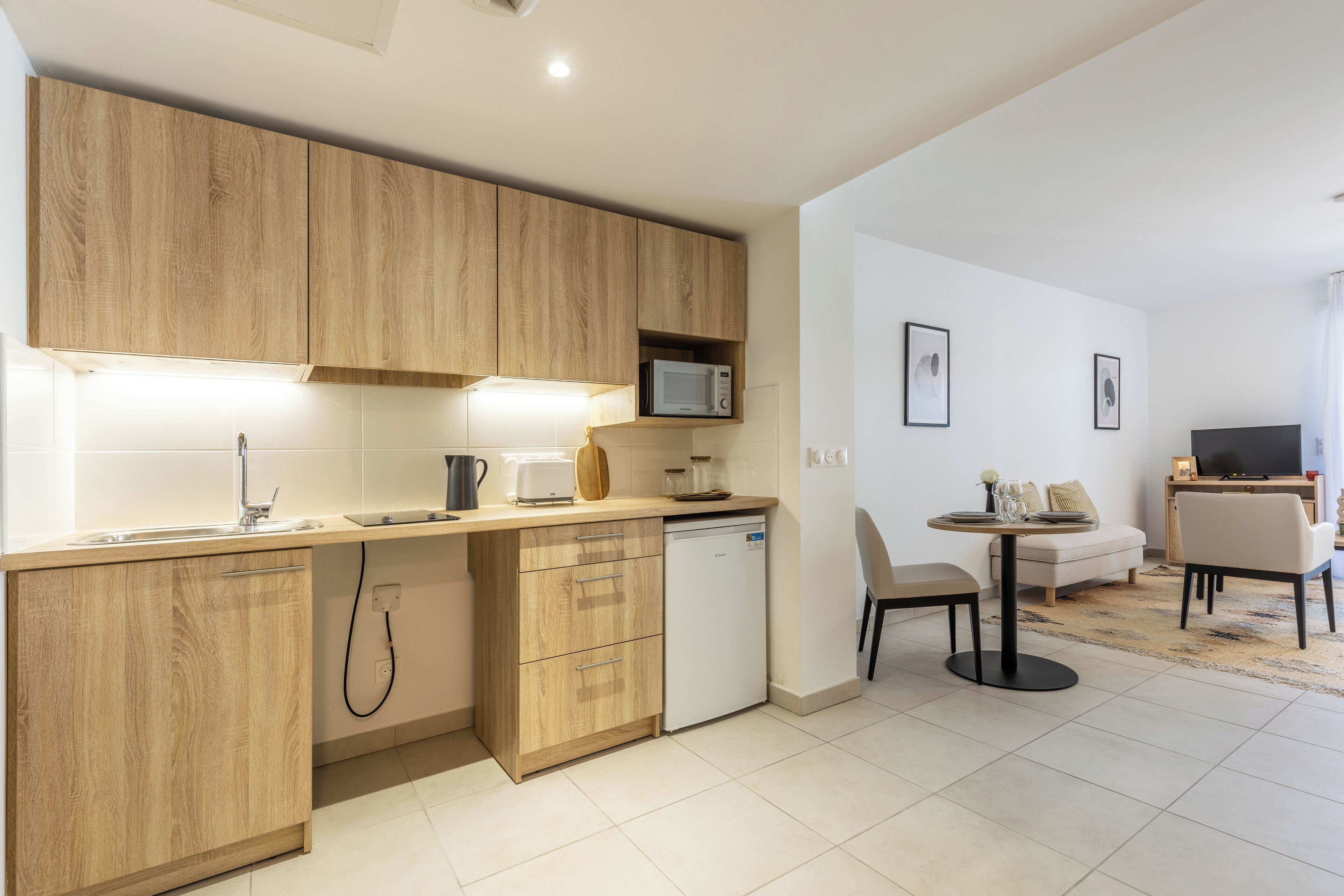 A modern kitchen with wooden cabinets, a microwave, and a dishwasher. There is a dining area with a table and chairs.