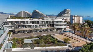 Un hôtel moderne à plusieurs étages, doté d’espaces extérieurs aménagés et offrant une vue sur la mer.