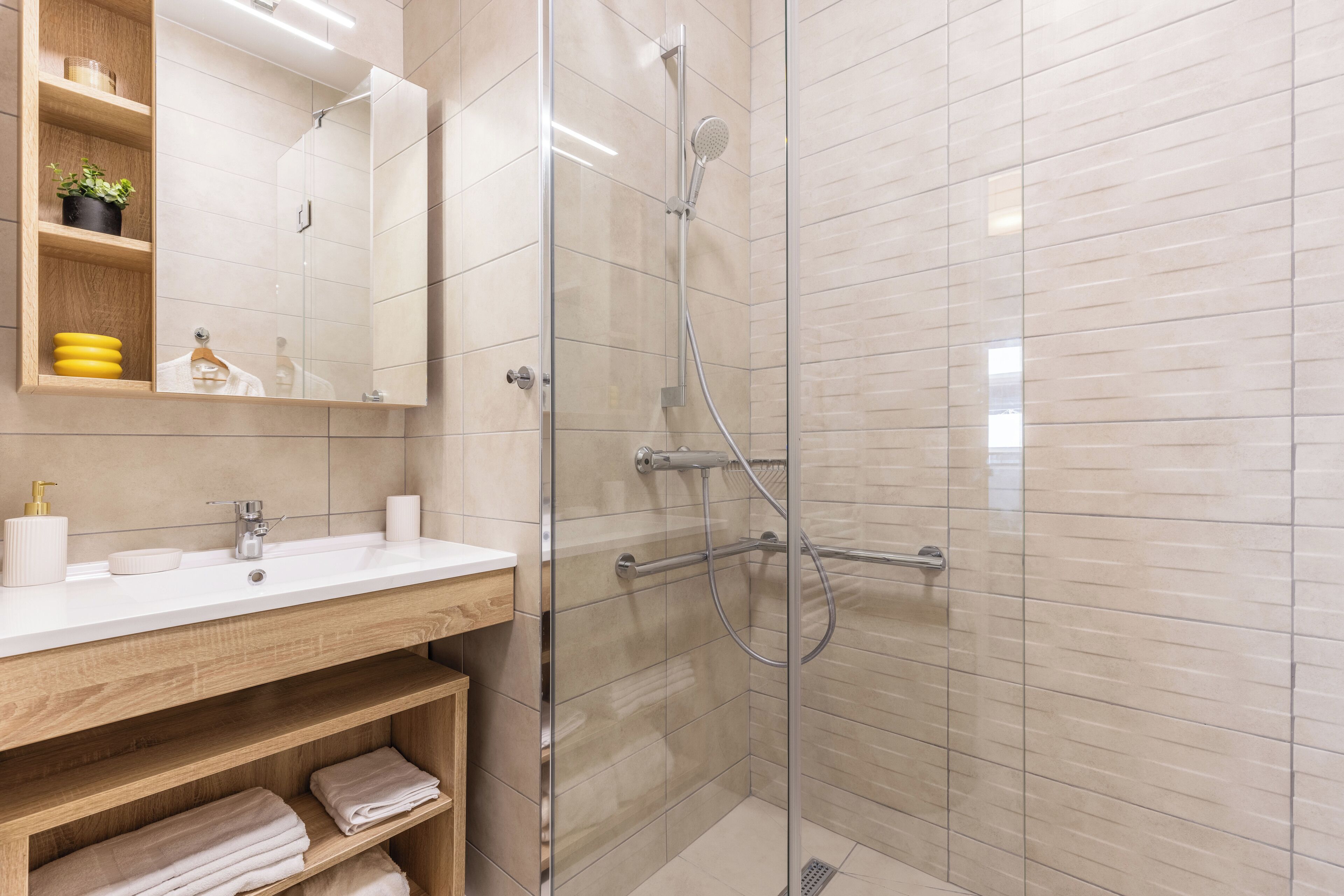 A modern bathroom with a glass-enclosed shower, a wooden vanity with a mirror, and a shelf with towels.