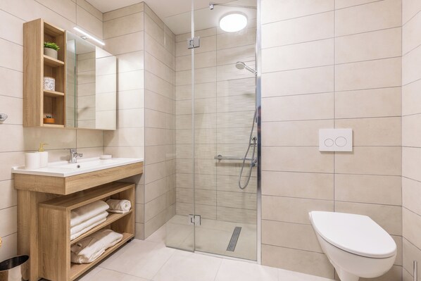 A modern bathroom with a glass-enclosed shower, a wooden vanity with a mirror, and a white toilet. - Zenao Appart'hôtels Villeneuve Loubet (Villeneuve-Loubet)