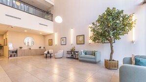 Un hall d’entrée spacieux avec un comptoir d’accueil, un espace salon et un grand arbre.