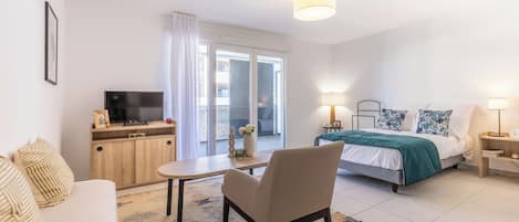 A modern bedroom with a bed, bedside tables, a TV, and a view through a sliding door.