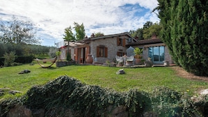 Uma casa de pedra com um jardim, uma rede e uma árvore grande.