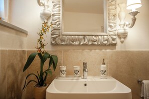 Ein Badezimmer mit Waschbecken, Spiegel, dekorativen Wandleuchten und einem Blumentopf.