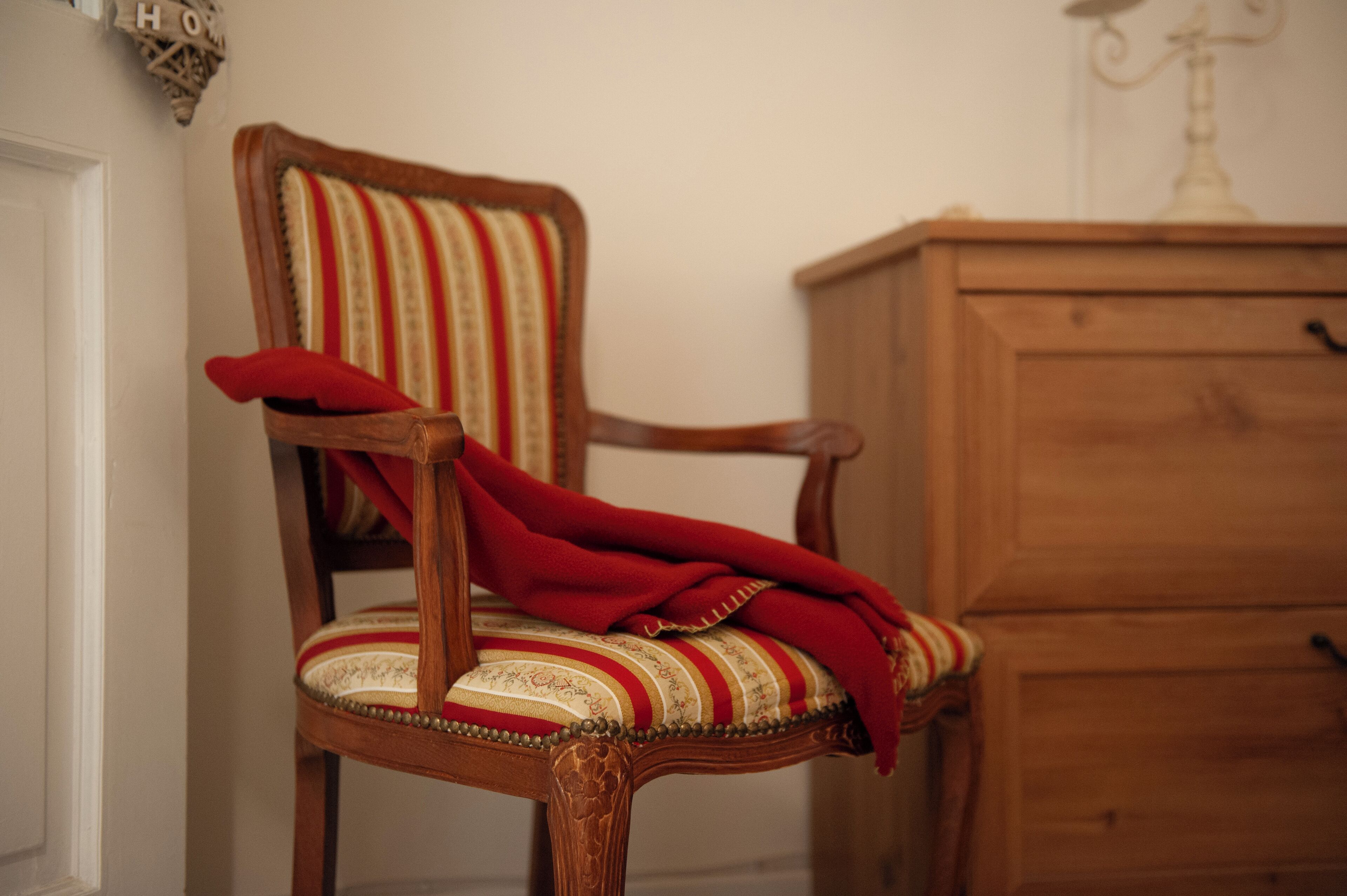 A wooden chair with a striped cushion and a red throw blanket.