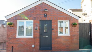A red brick house with a dark front door, two windows with white frames, and a small porch area. - Cosy Central Cardiff Bungalow (Cardiff)