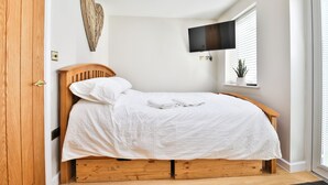 A bedroom with a wooden bed, white bedding, a mounted TV, and a window with blinds. - Cosy Central Cardiff Bungalow (Cardiff)