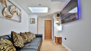A modern living room with a leather sofa, zebra-patterned cushions, a wall-mounted TV, and a skylight. - Cosy Central Cardiff Bungalow (Cardiff)