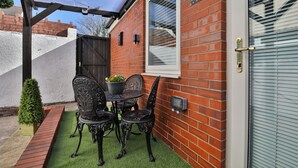 A patio with a table and chairs, a potted plant, and a brick wall. - Cosy Central Cardiff Bungalow (Cardiff)