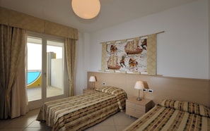 A hotel room with two single beds, a large window with curtains, a wall-mounted artwork, and a small bedside table with a lamp.