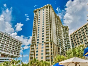 Un hôtel de grande hauteur doté de nombreux balcons, un ciel d’un bleu éclatant et des palmiers au premier plan.