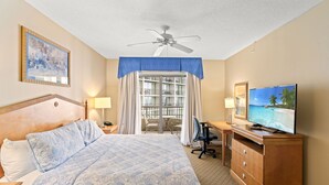 A hotel room with a large bed, a desk, a television, a ceiling fan, and a balcony with a view of the ocean. - Royale Palms 801H Oceanview Studio in Kingston (Myrtle Beach)