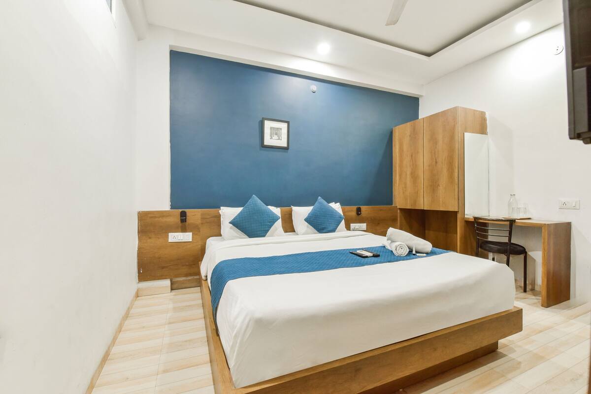 Una habitación de hotel moderna con una cama grande, cabecera de madera y una pared azul.