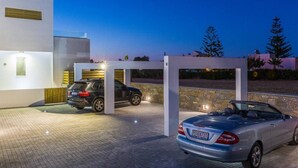 Un edificio moderno con una zona de estacionamiento techada, una camioneta SUV negra y un automóvil descapotable plateado.