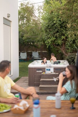 An outdoor hot tub with a control panel, surrounded by a wooden deck and a grassy yard.