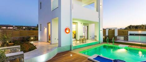 A modern two-story house with a swimming pool, outdoor seating, and a well-lit entrance.
