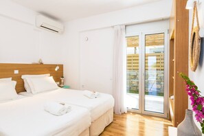 Une chambre d’hôtel équipée d’un lit, d’une table de chevet, d’une lampe, d’un climatiseur et donnant sur un espace extérieur grâce à une porte vitrée.