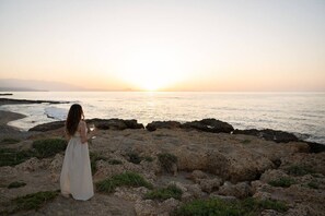 A person standing on rocky terrain overlooking a body of water during sunset.