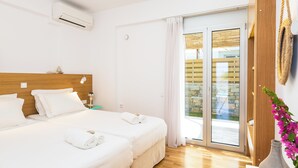 Une chambre d’hôtel avec deux lits, une tête de lit en bois, une grande porte-fenêtre coulissante donnant sur l’extérieur et un vase avec des fleurs sur le côté droit.