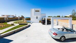 A modern building with a parking area, a car, and a clear blue sky. - Persi by the beach! Thalasses villas (Rethymno)