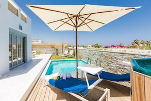 A rooftop pool area with a wooden deck, a lounge chair, a table with a blue tablecloth, and a hot tub. - Persi by the beach! Thalasses villas (Rethymno)