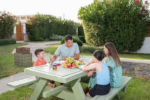 A family dining at an outdoor table with a garden view. - Persi by the beach! Thalasses villas (Rethymno)