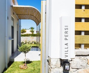 A villa entrance with a stone wall and a wooden fence.