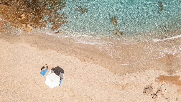 Une vue aérienne d’une plage aux eaux turquoise et limpides, avec un rivage sablonneux et des empreintes de pas.