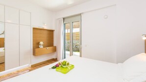 A modern bedroom with a bed, a built-in wardrobe, a small shelf, and a sliding glass door to the outside. - Persi by the beach! Thalasses villas (Rethymno)