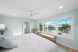 Ein Schlafzimmer mit einem großen Bett, einem Deckenventilator, einer Bank am Fenster und Blick auf ein Gewässer und eine Anlegestelle.