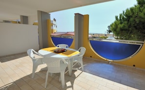 A patio with a round table and four chairs, a blue and yellow wall, and a view of buildings and trees.