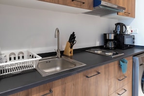 A modern kitchen with a stainless steel sink, a coffee maker, and wooden cabinets. - Bloomfields Studio in Oasis 1-Masdar (Abu Dhabi)
