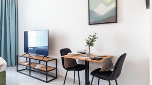 A modern dining area with a wooden table, black chairs, and a TV on a stand. - Bloomfields Euphoric STU in Oasis Masdar (Abu Dhabi)