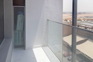 A balcony with a glass railing overlooking a parking area and distant buildings. - Bloomfields Studio in Oasis 1-Masdar (Abu Dhabi)