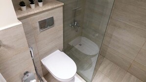 A modern bathroom with a glass-enclosed shower, a toilet, and a shelf with potted plants. - Bloomfields Euphoric STU in Oasis Masdar (Abu Dhabi)